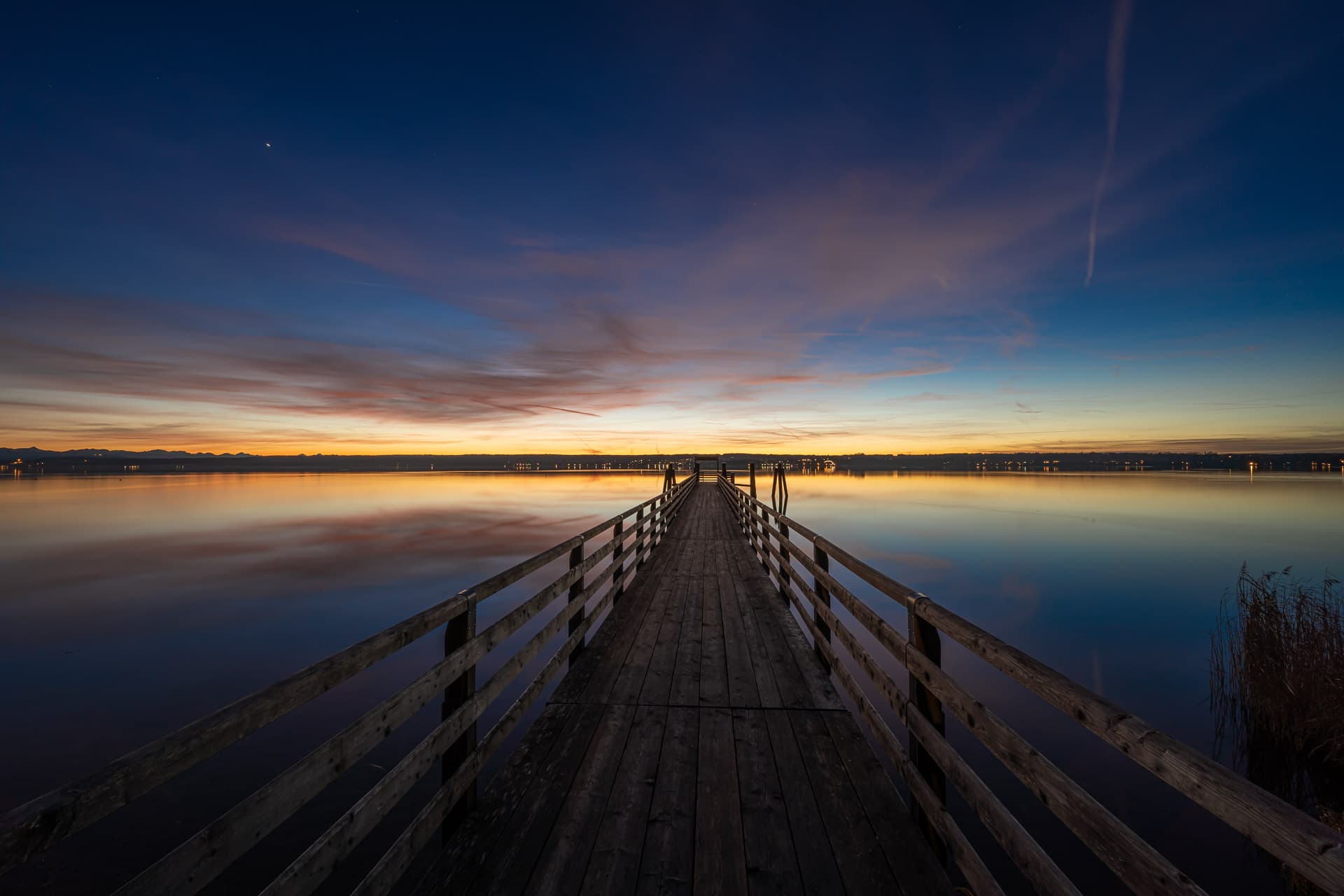 A wooden jetty reaching into Lake Ammersee at sunset